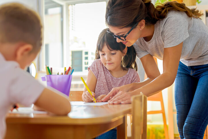 early childcare assistant helping a student with their writing