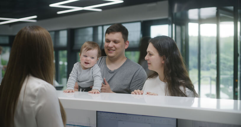 A Medical Office Administrator at a clinic reception assisting a young family, exemplifying patient interaction, one of the many duties of a Medical Office Administrator